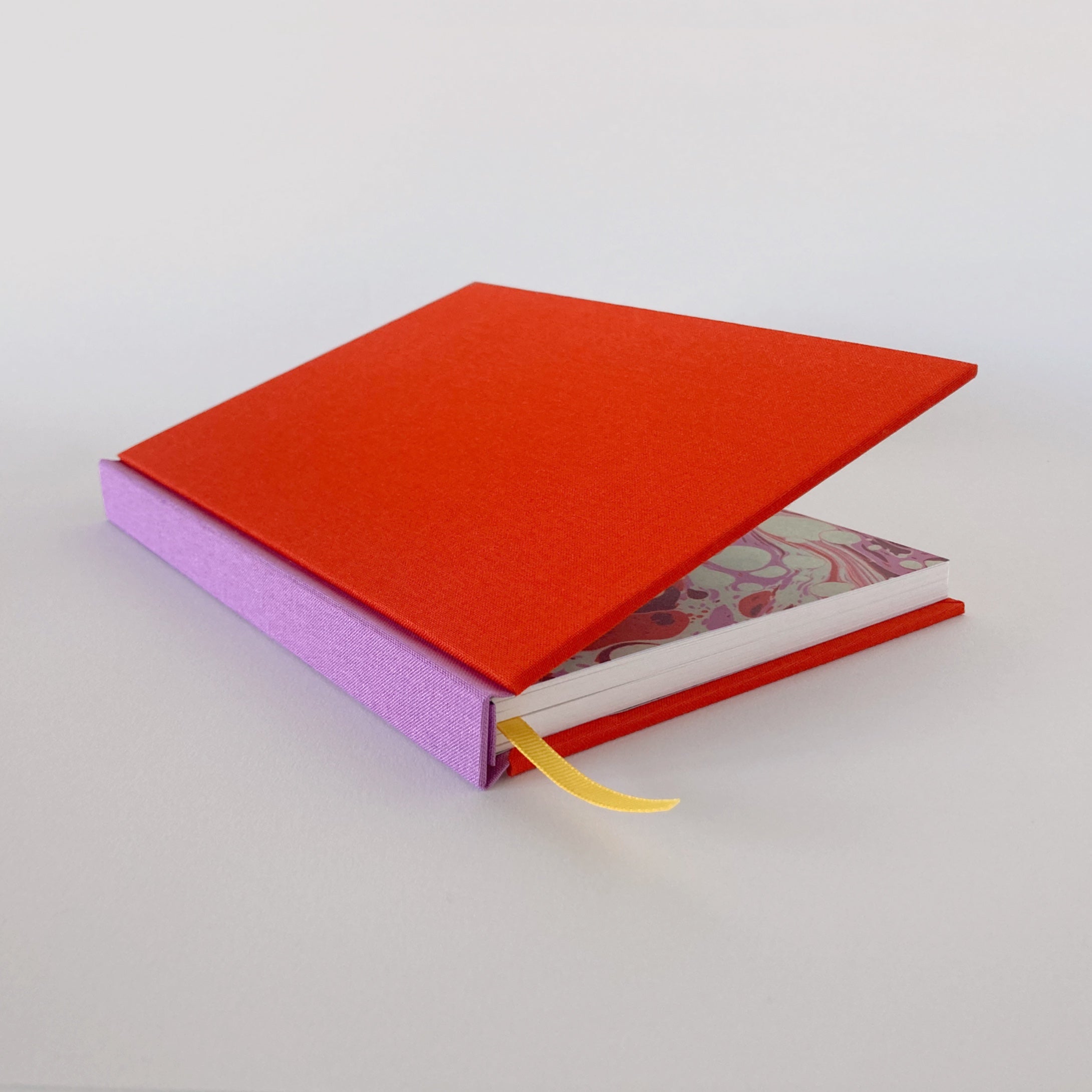 Red and pink hardback sketchbook partially open, revealing marble endpapers.