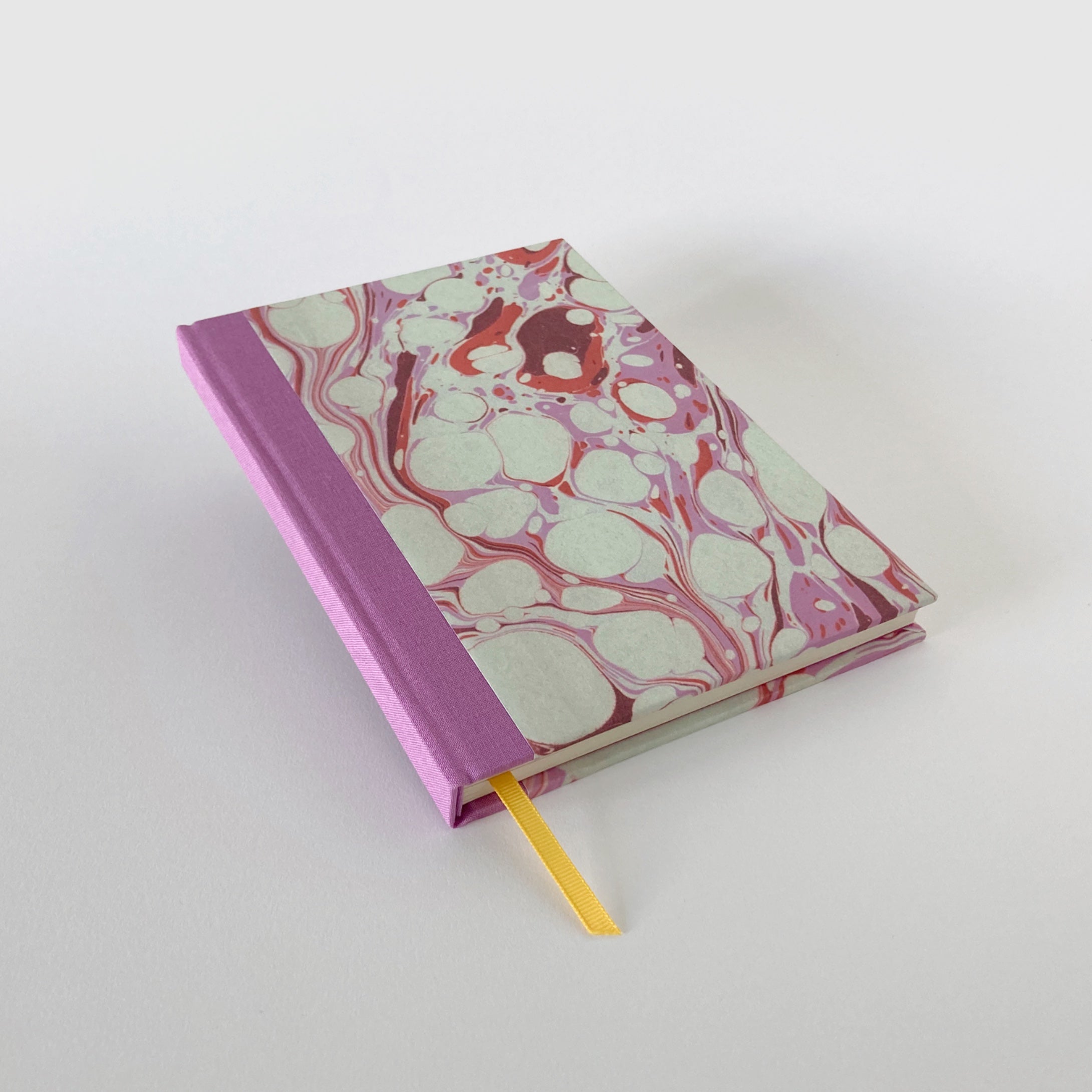Pink marble hardback notebook with cloth spine and yellow ribbon bookmark.