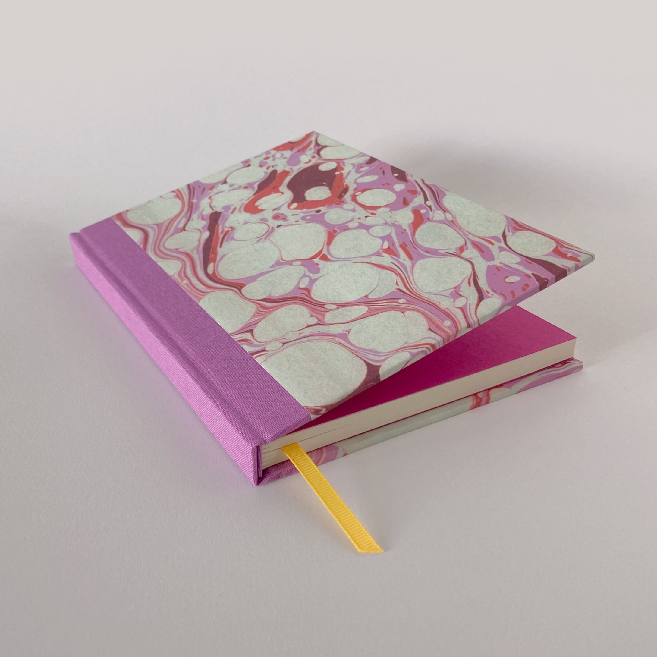 Pink marble hardback notebook partially open, revealing pink end pages.